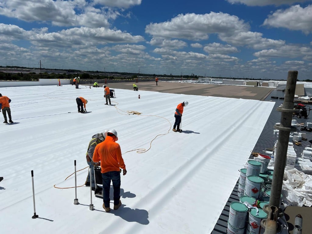 Capstone crew installing white TPO membrane on a commercial roof