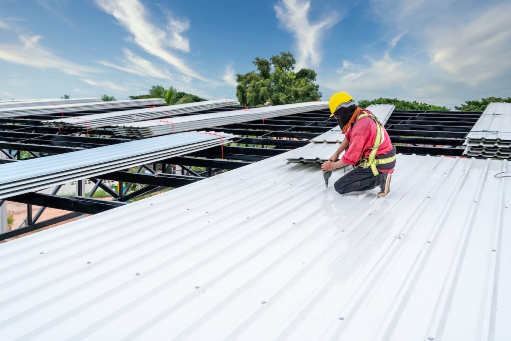 A Roofer Construction worker install new roof, Electric drill used on new roofs with white Metal Sheet. Working at height equipment.
