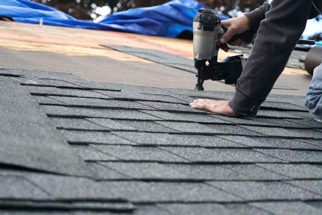 handyman using nail gun to install shingle to repair roof