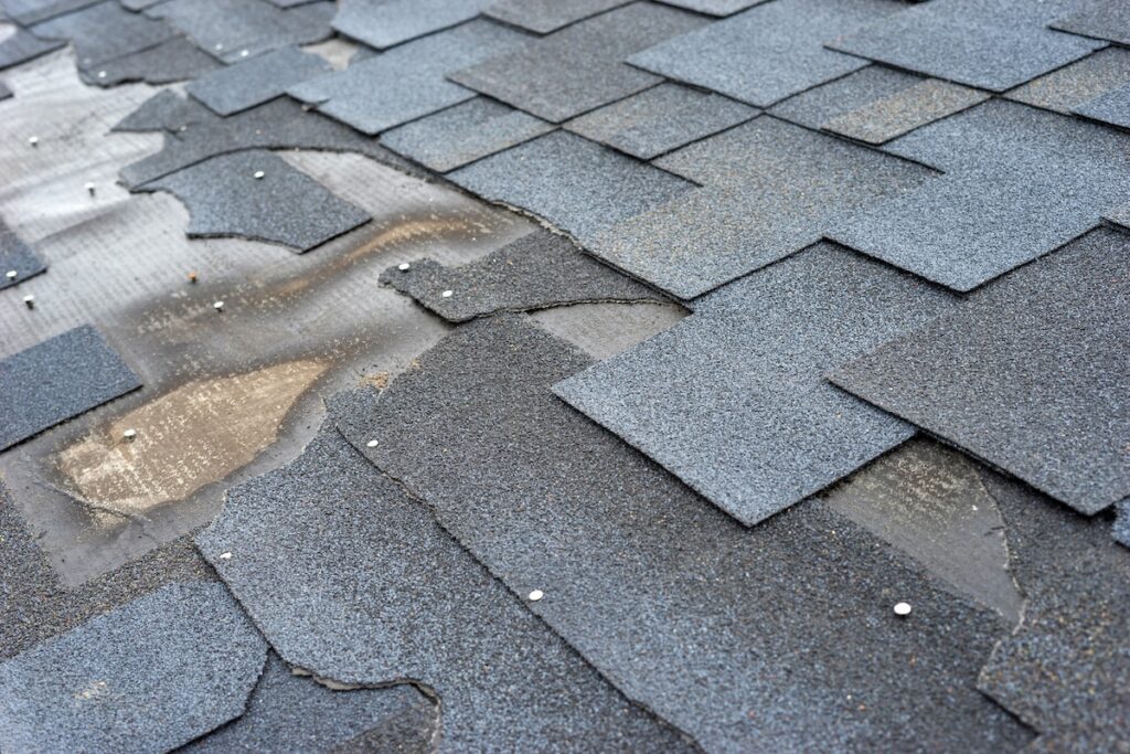 Сlose up view of bitumen shingles roof damage that needs repair.