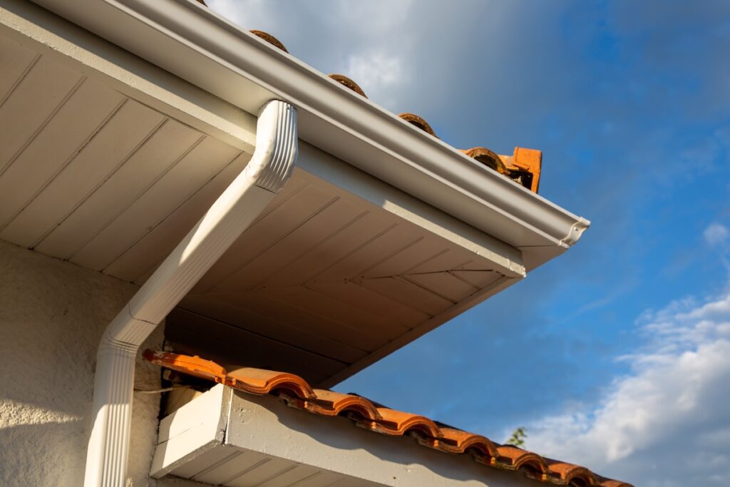 House corner with white planks siding and roof with steel seamless gutter installed