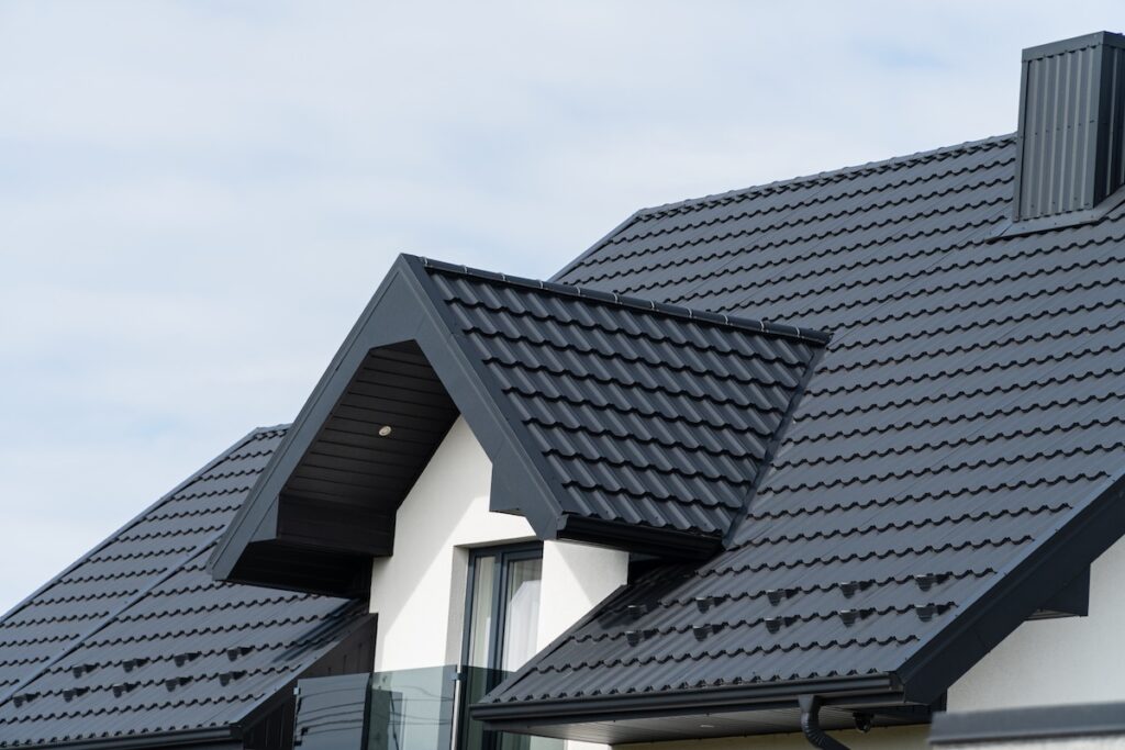 A beautiful modern house is covered with black metal tiles. Roofing of metal profile wavy shape.