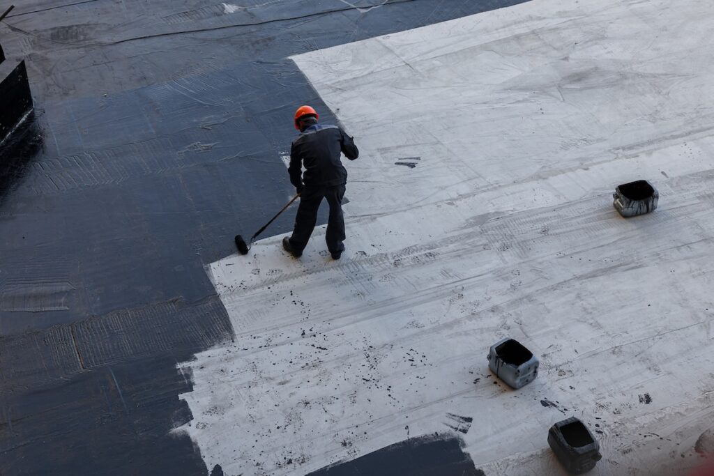 Waterproofing coating. A worker applies bitumen mastic to the foundation. Roofer cover the waterproofing primer on the roof, modified with polymer bitumen, with a roller brush.