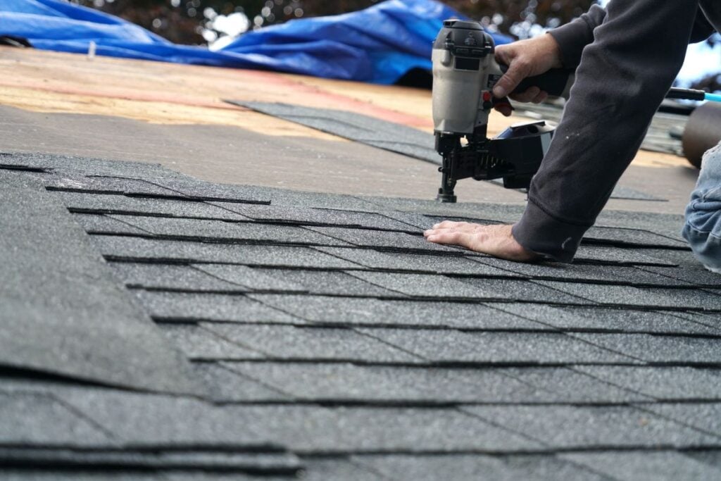 roofer using a nail gun to install new shingles