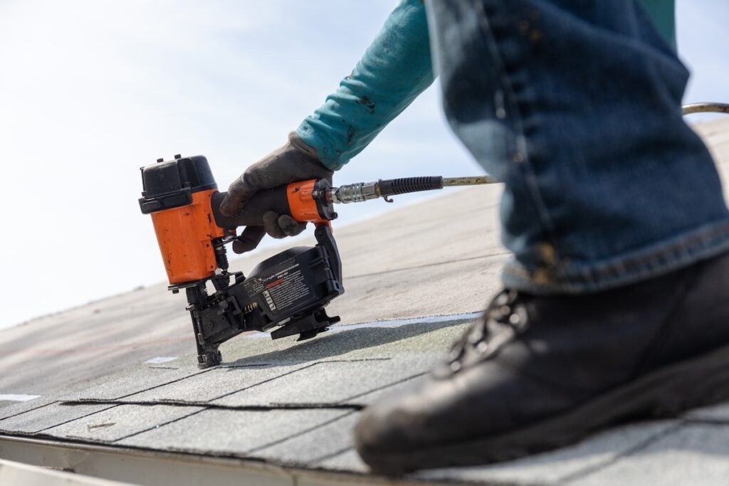 roofer installing roof shingles with pnuematic roofing nailer.