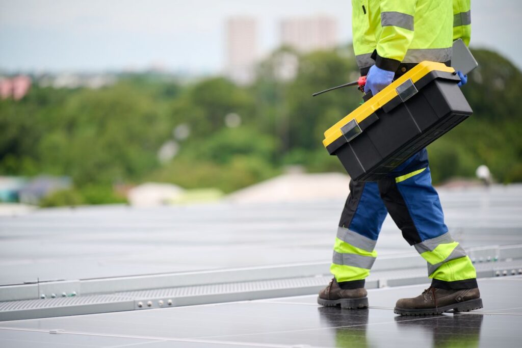 commercial roof inspection worker walking on top of roof holding toolbox