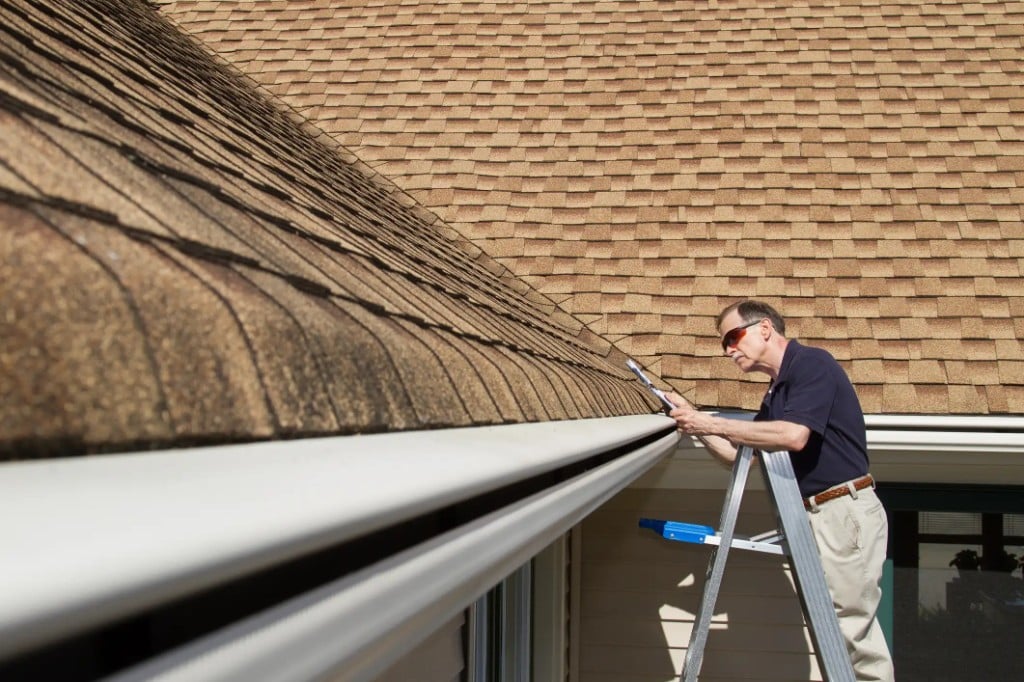 Capstone inspector on a ladder checking gutters and the roof of a North Bay home